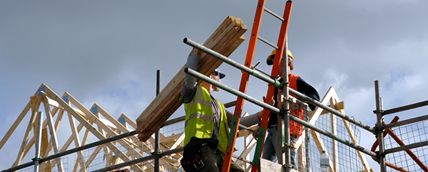 Man carrying wood planks on scaffolding.